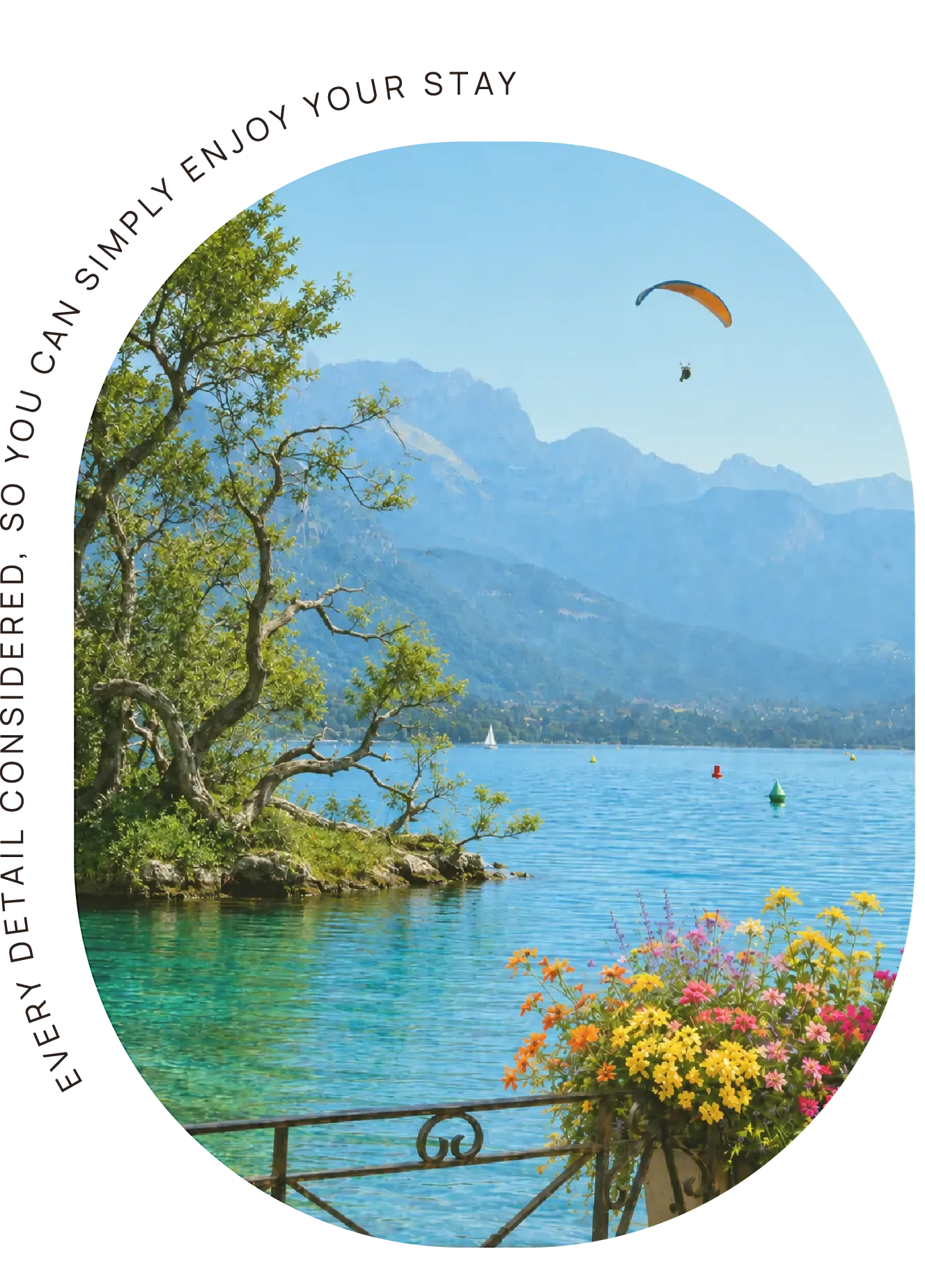View of Lake Annecy with mountains, flowers in the foreground and a paraglider in the sky